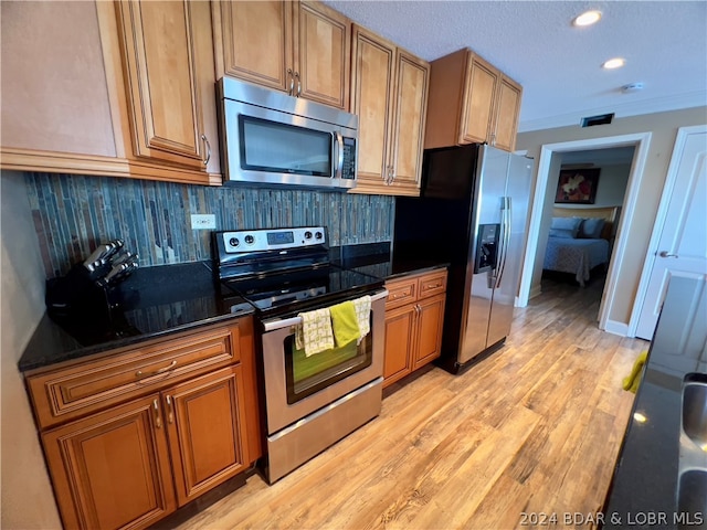 kitchen featuring stainless steel appliances, light hardwood / wood-style floors, backsplash, and dark stone counters