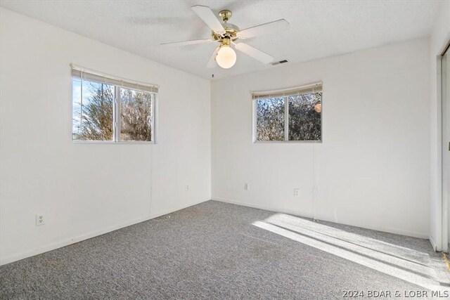 empty room with carpet flooring, ceiling fan, a healthy amount of sunlight, and a textured ceiling