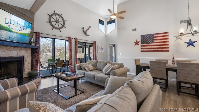 living room featuring ceiling fan with notable chandelier, high vaulted ceiling, dark wood-type flooring, and a stone fireplace