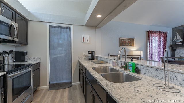 kitchen with sink, stainless steel appliances, light wood-type flooring, and light stone counters