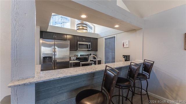 kitchen with vaulted ceiling, a breakfast bar area, stainless steel appliances, and light stone counters