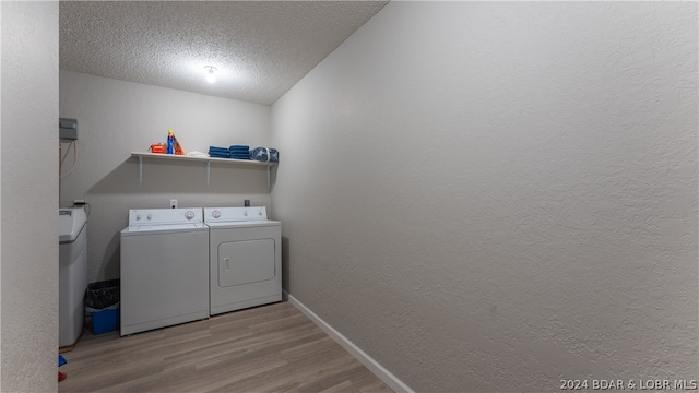 clothes washing area featuring washer and clothes dryer, a textured ceiling, and light wood-type flooring