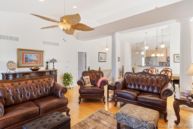 living room featuring ceiling fan, ornate columns, a towering ceiling, and light wood-type flooring