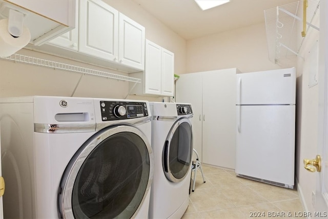 clothes washing area featuring washing machine and clothes dryer, cabinets, and light tile floors