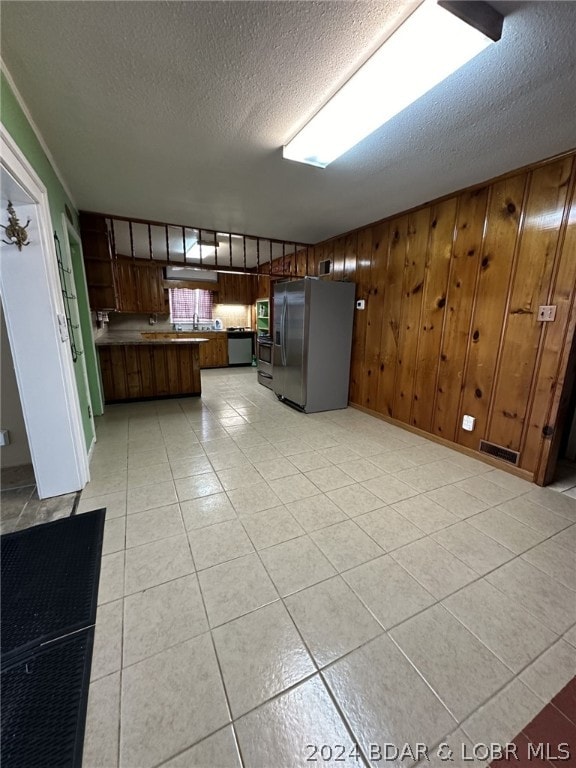 kitchen featuring stainless steel appliances, wooden walls, a textured ceiling, and light tile floors