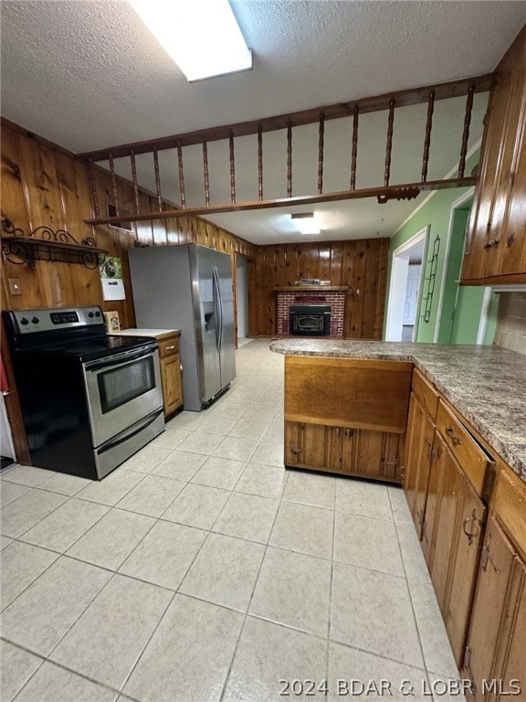 kitchen featuring stainless steel appliances, a fireplace, a textured ceiling, light tile floors, and wooden walls