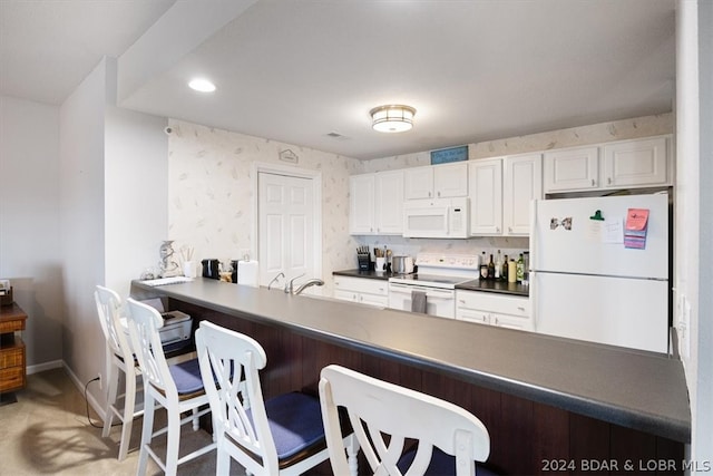 kitchen with white appliances, a kitchen bar, light carpet, and white cabinetry