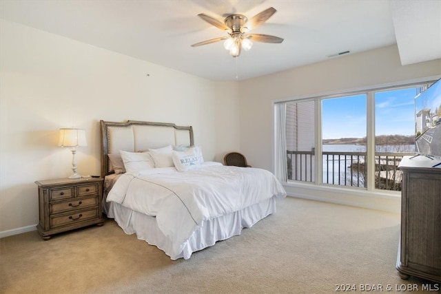 bedroom featuring light carpet, a water view, and ceiling fan