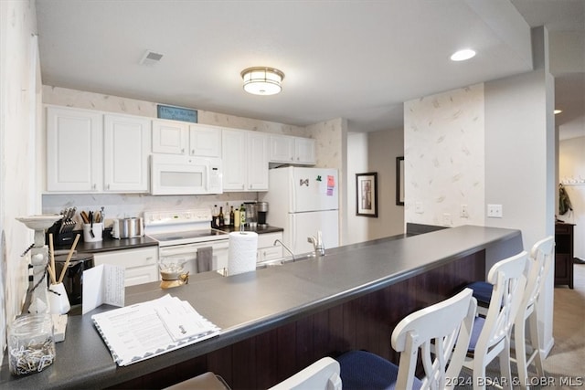 kitchen featuring light colored carpet, a kitchen bar, kitchen peninsula, white appliances, and white cabinets