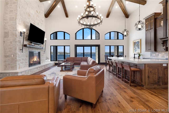 living room featuring dark hardwood / wood-style floors, a high ceiling, an inviting chandelier, beam ceiling, and a stone fireplace