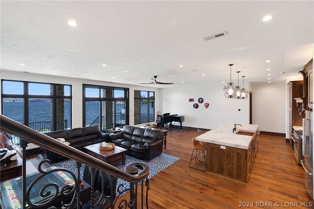 living room featuring ceiling fan, a water view, a textured ceiling, sink, and dark hardwood / wood-style floors