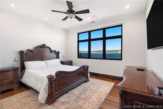 bedroom featuring dark hardwood / wood-style flooring, ceiling fan, and a water view