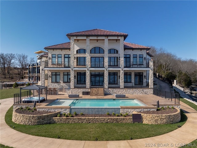 rear view of property featuring a pool with hot tub, a patio area, and a balcony