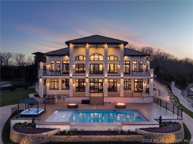 back house at dusk with a patio, a swimming pool with hot tub, and a balcony