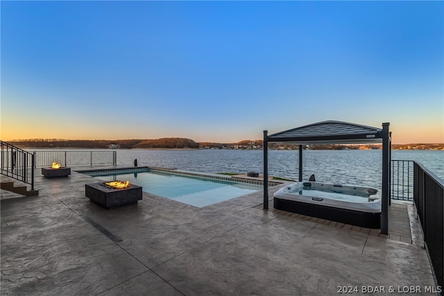 pool at dusk with a patio, an outdoor fire pit, an outdoor hot tub, and a water view