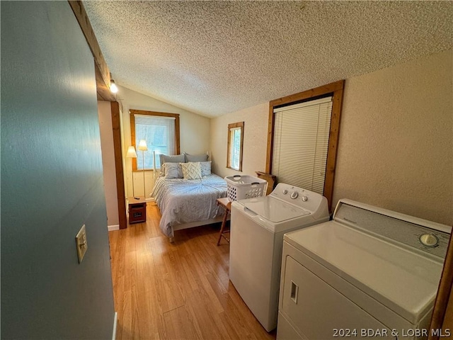 bedroom with vaulted ceiling, washer and dryer, a textured ceiling, and light hardwood / wood-style flooring