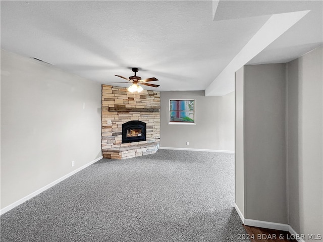 unfurnished living room featuring a textured ceiling, dark colored carpet, ceiling fan, and a stone fireplace