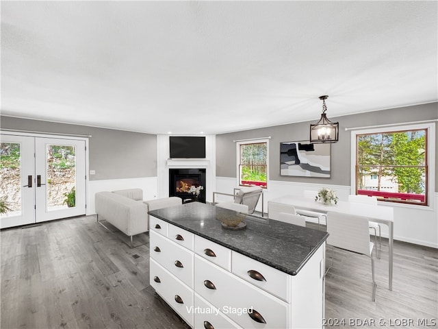 kitchen with a kitchen island, dark stone counters, white cabinetry, hardwood / wood-style floors, and pendant lighting