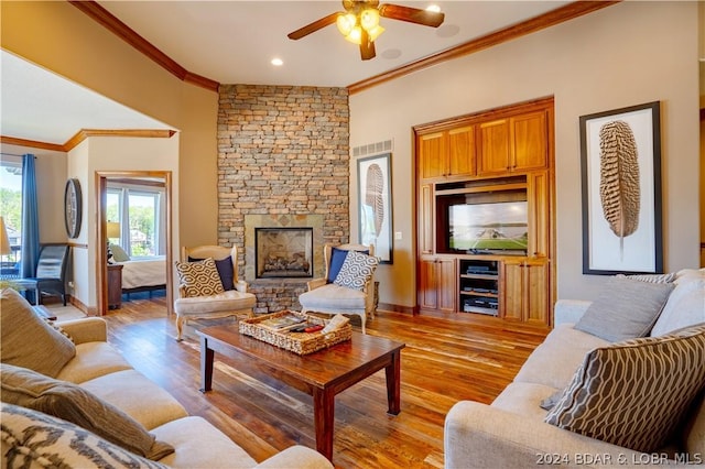 living room featuring crown molding, a stone fireplace, light hardwood / wood-style floors, and ceiling fan