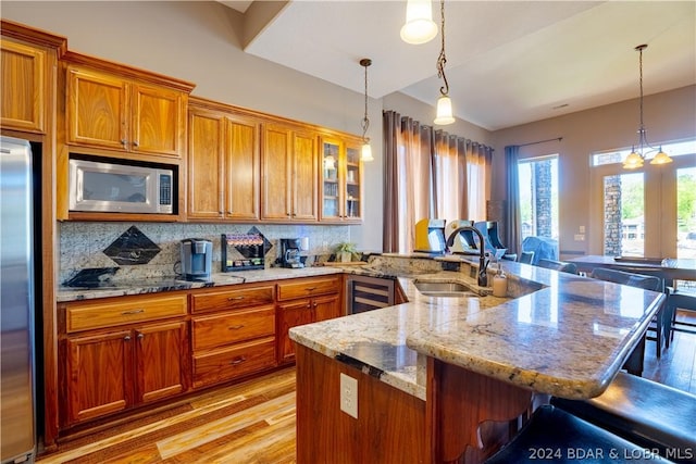 kitchen featuring sink, decorative light fixtures, appliances with stainless steel finishes, a kitchen breakfast bar, and light stone countertops