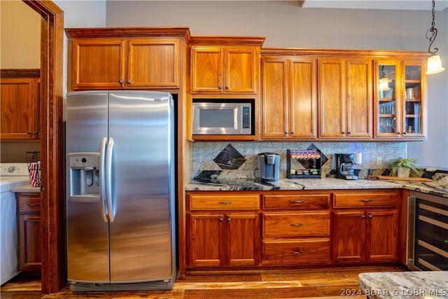 kitchen featuring decorative light fixtures, washer / dryer, beverage cooler, stainless steel appliances, and light stone countertops