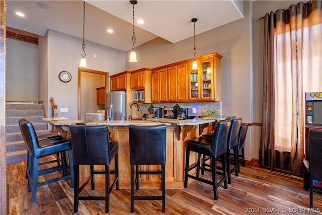 kitchen with appliances with stainless steel finishes, washing machine and dryer, dark hardwood / wood-style floors, decorative backsplash, and kitchen peninsula