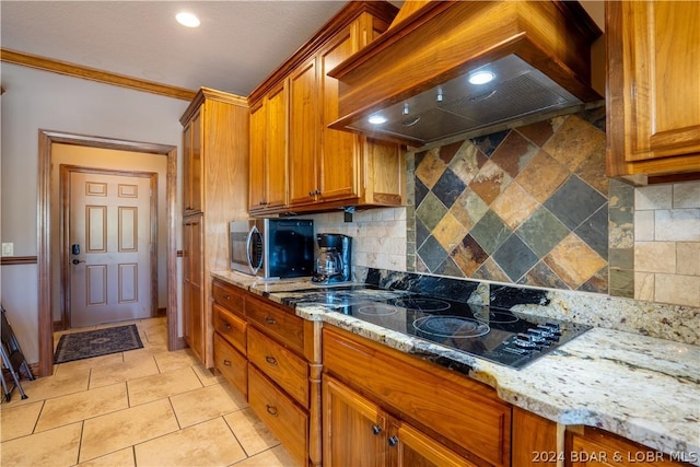 kitchen with tasteful backsplash, black electric stovetop, light stone countertops, and custom range hood