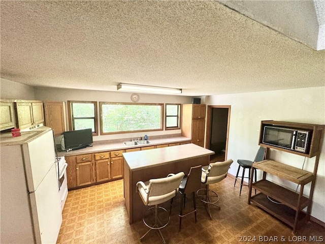 kitchen featuring a breakfast bar area, white appliances, a textured ceiling, a center island, and sink