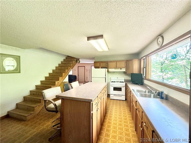 kitchen with white appliances, a breakfast bar, sink, a kitchen island, and a textured ceiling