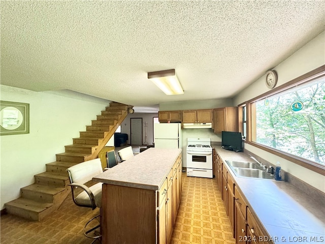 kitchen featuring a textured ceiling, white appliances, sink, a center island, and a breakfast bar area