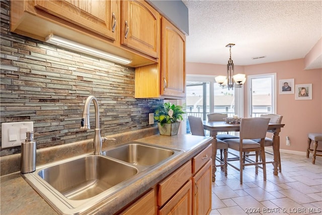 kitchen featuring backsplash, baseboards, decorative light fixtures, a textured ceiling, and a sink