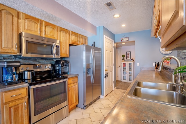 kitchen featuring backsplash, a textured ceiling, stainless steel appliances, sink, and light tile patterned flooring