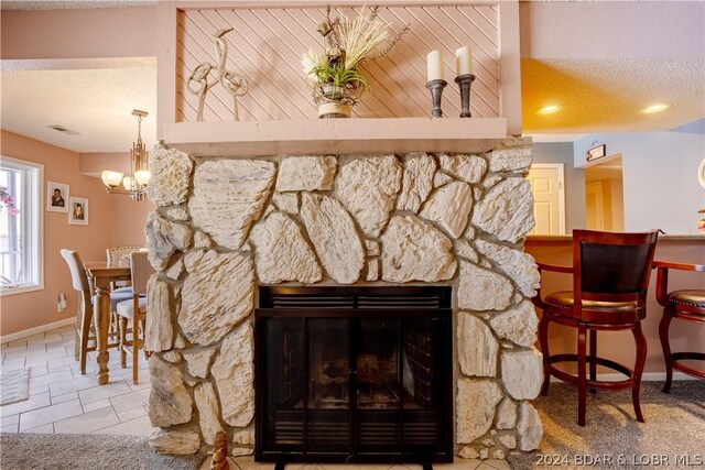 details featuring a notable chandelier, a stone fireplace, and a textured ceiling