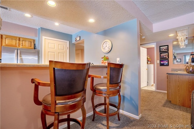 bar featuring stainless steel refrigerator, light colored carpet, and a textured ceiling