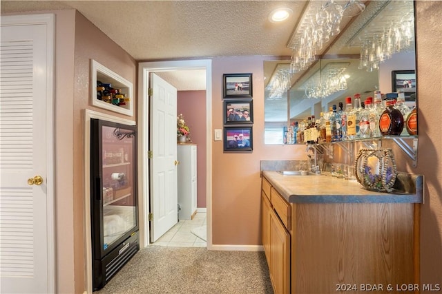 bar with light carpet, a sink, a textured ceiling, indoor wet bar, and baseboards