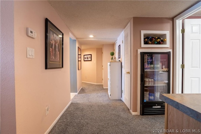 corridor with carpet flooring, a textured ceiling, and wine cooler