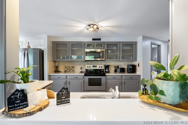 kitchen featuring appliances with stainless steel finishes, gray cabinets, a textured ceiling, tasteful backsplash, and sink