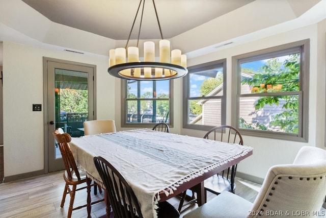 dining area with an inviting chandelier, plenty of natural light, light hardwood / wood-style flooring, and a raised ceiling