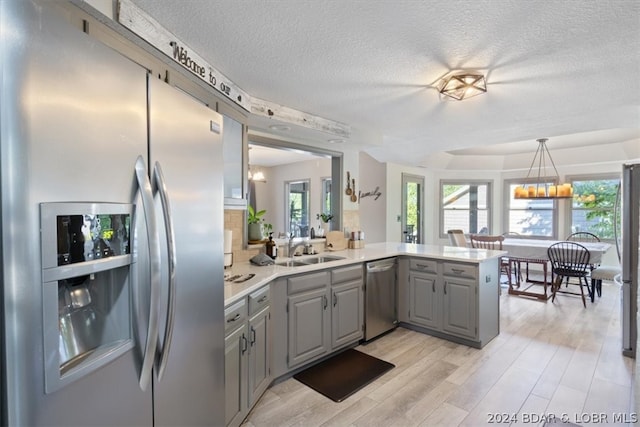 kitchen with pendant lighting, gray cabinetry, light hardwood / wood-style flooring, kitchen peninsula, and stainless steel appliances