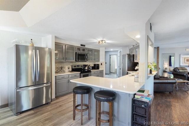 kitchen with gray cabinetry, appliances with stainless steel finishes, wood-type flooring, and kitchen peninsula