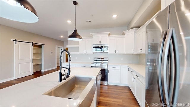 kitchen featuring decorative light fixtures, a barn door, white cabinetry, appliances with stainless steel finishes, and sink