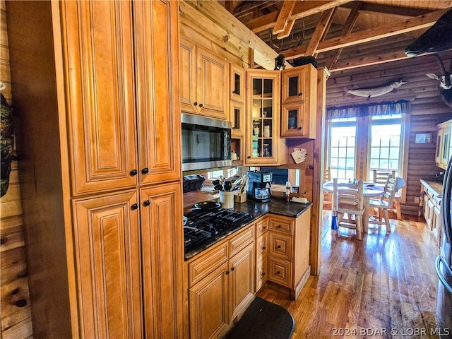 kitchen with light hardwood / wood-style floors, lofted ceiling with beams, rustic walls, and black gas stovetop