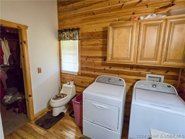 laundry room with wooden walls, washer and dryer, and light hardwood / wood-style floors