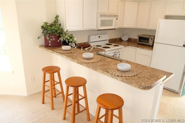 kitchen with white appliances, white cabinetry, a peninsula, a toaster, and a kitchen bar