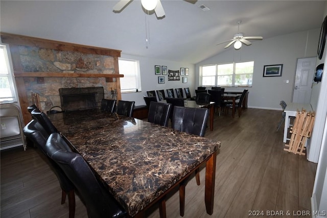 dining room with vaulted ceiling, dark hardwood / wood-style floors, a stone fireplace, and ceiling fan