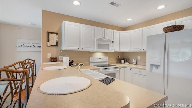 kitchen featuring white appliances, white cabinetry, kitchen peninsula, and sink