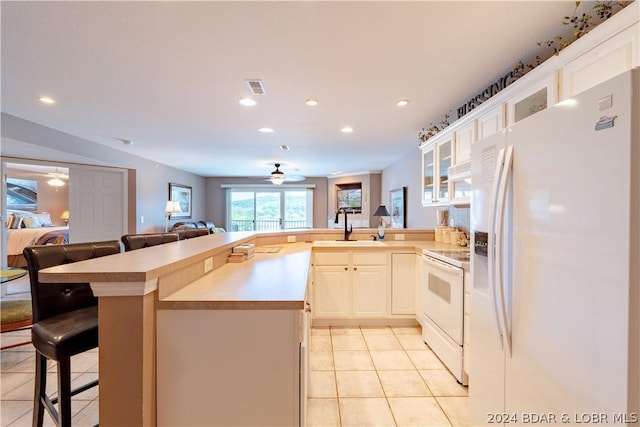 kitchen featuring sink, kitchen peninsula, white appliances, a breakfast bar area, and light tile patterned floors