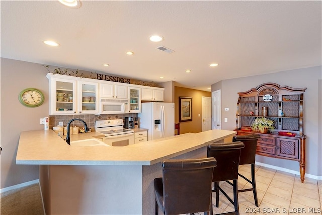 kitchen featuring white appliances, white cabinets, sink, kitchen peninsula, and a breakfast bar area