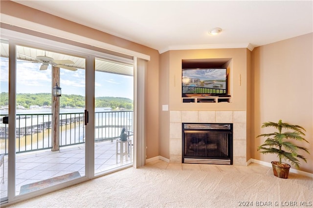 carpeted living room with ceiling fan, a water view, and a tiled fireplace