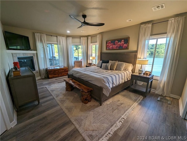 bedroom featuring ceiling fan, dark hardwood / wood-style flooring, a tiled fireplace, and multiple windows